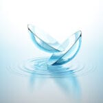 Due lenti a contatto trasparenti si sfiorano sopra acqua calma, con riflessi ...