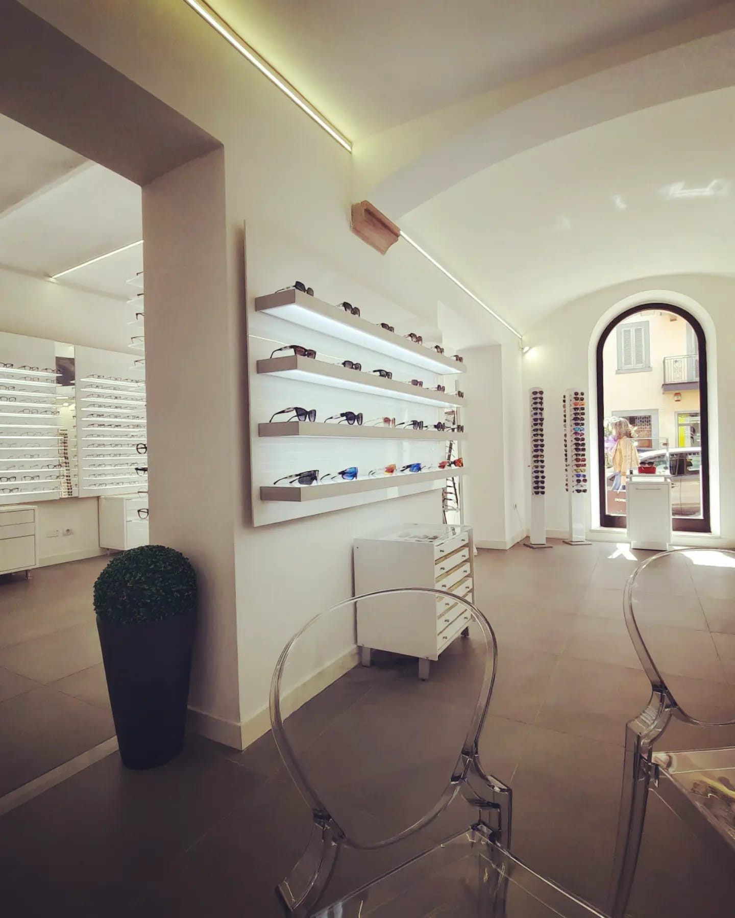 Negozio di occhiali moderno con pareti bianche, sedie trasparenti, vetrina ad...