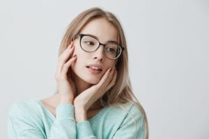 Giovane donna bionda con occhiali e maglione azzurro guarda serena di lato, m...