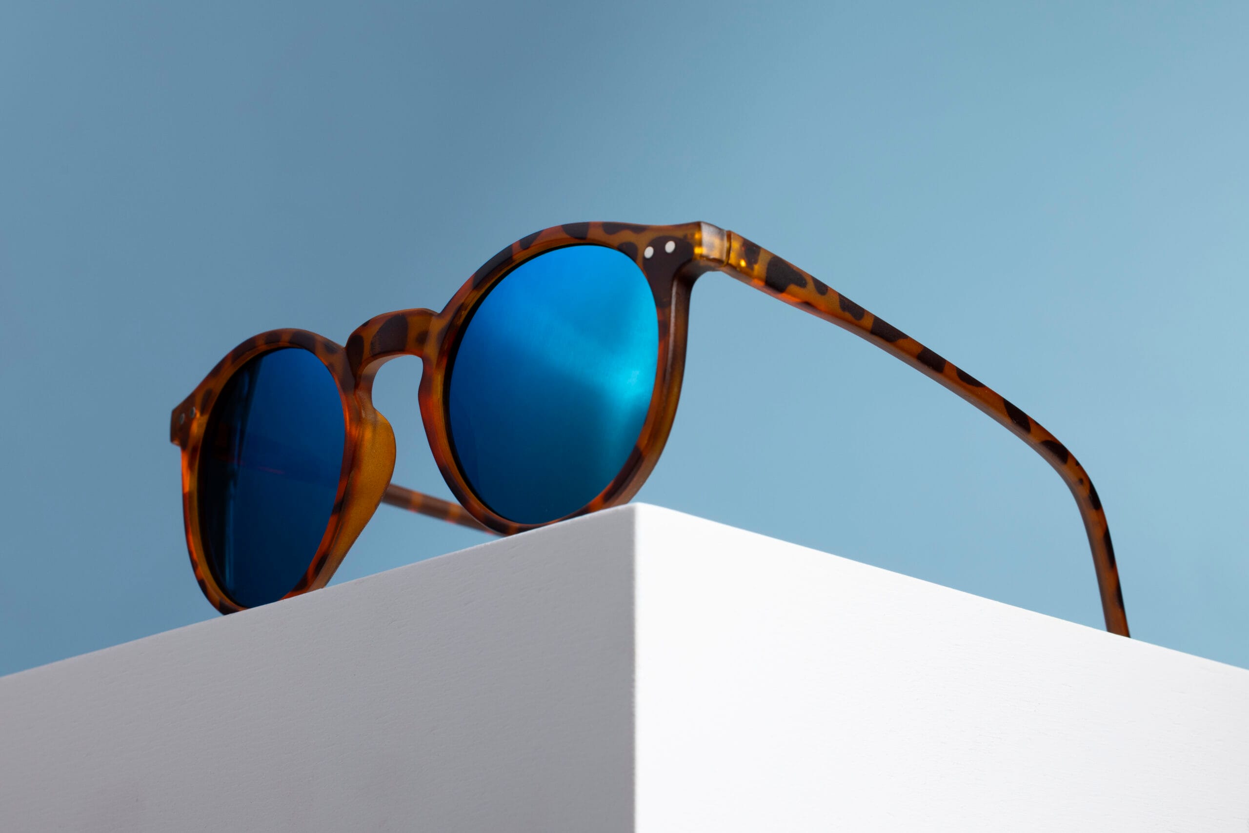 Occhiali da sole tartarugati con lenti blu specchiate su una superficie bianc...