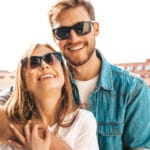 Coppia sorridente con occhiali di qualità all'aperto; lei davanti, lui l'abb...